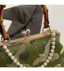 Close-up of green embroidery shoulder bag with bamboo handle and pearl chain detail