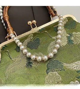 Close-up of green embroidered handbag featuring bamboo handle and crane pattern