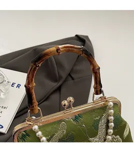 Detail of green satin bag with crane embroidery, bamboo handle and pearl strap