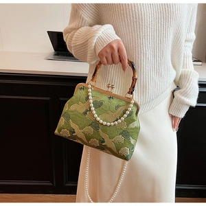 Detailed embroidery of cranes on a green silk bag with a bamboo handle and pearl chain