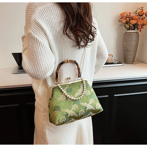 Detail of green satin embroidery bag with crane pattern and bamboo handle on model