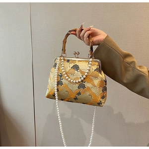 Close-up of golden embroidery crane bag with bamboo handle and pearl chain details