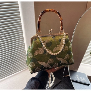 Detailed close-up of dark green silk embroidery handbag with bamboo handle and crane pattern