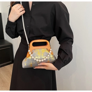 Détail du sac en tissu gris avec accents dorés, poignée en bois et bandoulière perle