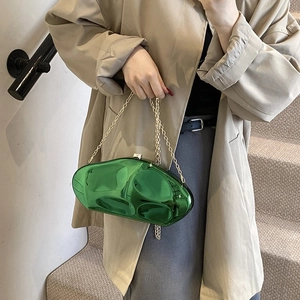 Metallic green cloud bag with gold chain strap worn over a khaki trench coat