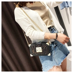 Detalle de bolso de mano rígido con lentejuelas negras, esquinas doradas y asa de cadena