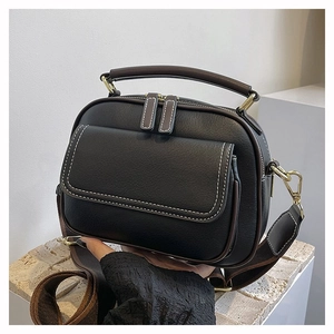 Detailansicht der schwarzen Ledertasche mit braunem Griff und weißen Kontrastnähten