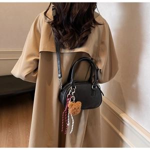 Detail of a black mini bowling bag with a cute bear pendant on a khaki trench coat