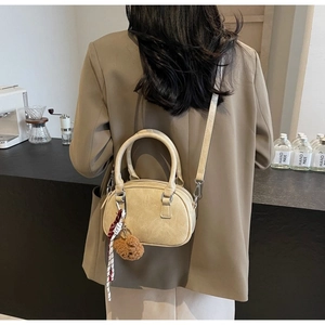 Chic cream leather handbag with teddy bear charm shown on model in a cafe setting