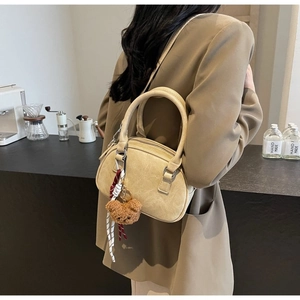 Detail of a beige Boston bag with vintage leather texture and cute teddy bear pendant