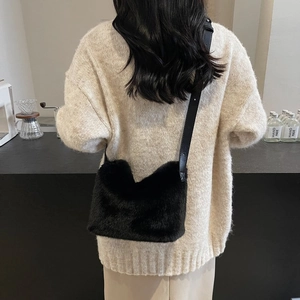 Detail of soft black faux fur shoulder bag worn with a white knit sweater in a cafe