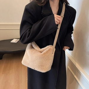 Close-up of beige plush crossbody bag with leather strap on a model wearing a black coat