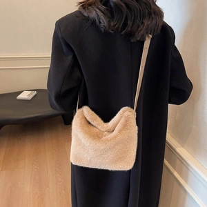 Detail of a beige plush crossbody bag with a slim leather strap on a black coat