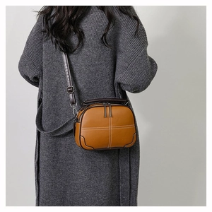 Detail view of caramel crossbody bag featuring white stitching and dual zip closure