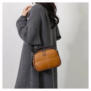 Detail view of brown leather crossbody bag with white cross-stitching and dark piping