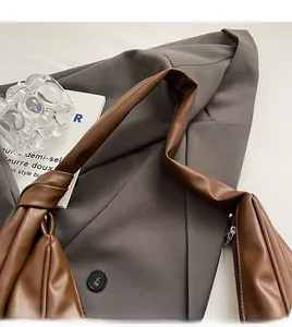 Detail of a brown leather shoulder bag with a stylish knotted strap on a gray blazer