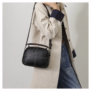 Retro black leather crossbody bag with white stitching detail worn with a beige trench coat