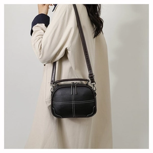 Detail of black crossbody bag with white stitching worn with a beige trench coat