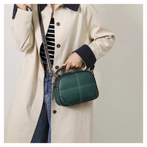Close-up of a dark green crossbody bag featuring white contrast stitching and grainy texture
