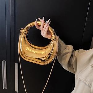 Détail d'un sac de soirée doré avec poignée anneau et bandoulière en chaîne fine