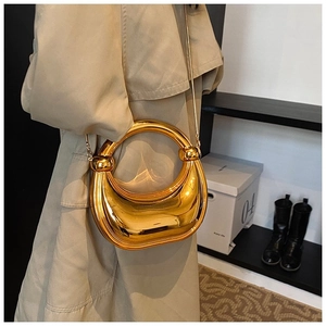 Détail d'un sac demi-lune doré avec poignée ronde et bandoulière chaîne sur un trench-coat kaki