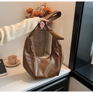 Close-up of brown PU leather dumpling bag with decorative knot and crescent design