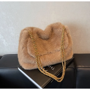 Detail of camel faux fur shoulder bag with gold chain strap on a black book