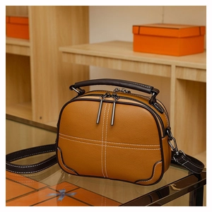 Detail view of brown leather crossbody bag with white contrast stitching and dual zippers