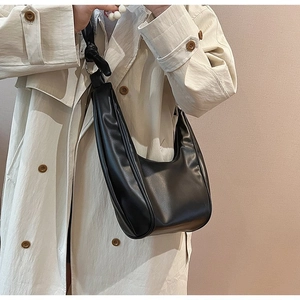 Detail of a black crescent shoulder bag with a stylish knotted strap and glossy finish