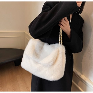 Detail of white faux fur tote bag with metal chain strap worn on black wool coat