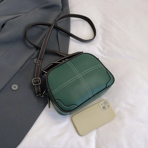 Detail of dark green crossbody bag with white stitching and leather handles