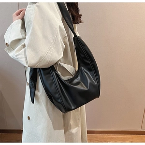 Side view of black crescent moon shoulder bag paired with a classic beige trench coat