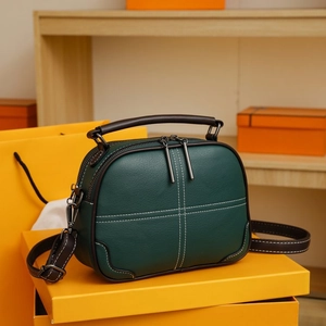 Detail of dark green lychee leather bag with white cross-stitching and brown handles