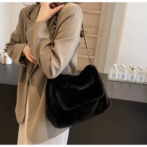 Detail of black faux fur shoulder bag with elegant metal chain strap on model