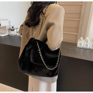Detail of black faux fur shoulder bag featuring premium gold chain strap on a model