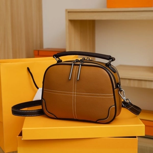 Detail of a brown leather crossbody bag with white cross-stitching on a yellow gift box
