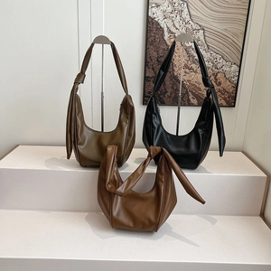 Three minimalist hobo bags in olive, black, and tan leather with knotted straps on display
