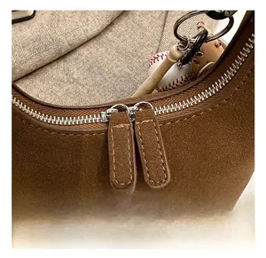 Détail de la double fermeture éclair en métal sur un sac en daim marron avec breloque