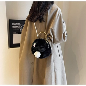Détail du sac lapin en peluche noire avec chaîne perle et broderie sur un trench-coat