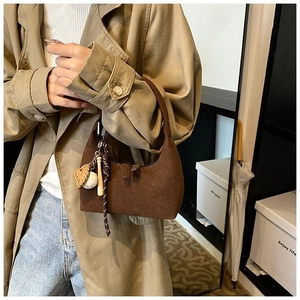 Gros plan du sac croissant en daim marron avec breloques de baseball et détails zippés