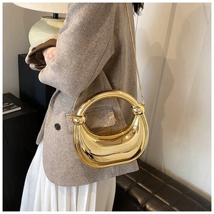 Sac de soirée doré en demi-lune avec poignée ronde et chaîne, porté avec un blazer élégant