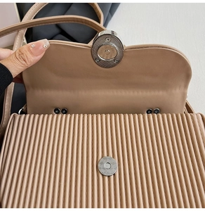 Close-up of beige pleated handbag featuring a silver magnetic clasp closure detail