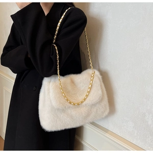 White plush shoulder bag with golden chain strap worn over a black winter coat