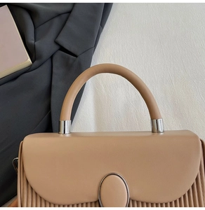 Detailed close-up of pleated texture and silver metallic buckle on beige handbag