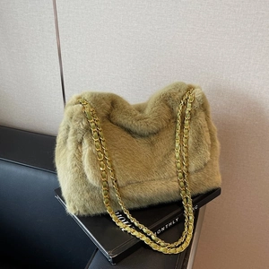 Olive green plush tote bag with gold chain strap placed on a book in a minimalist setting
