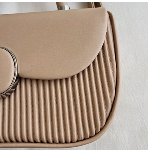 Detail of beige pleated crossbody bag showing vertical stripe texture and metal buckle