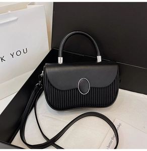 Close-up of black pleated leather handbag with silver oval buckle in a gift box