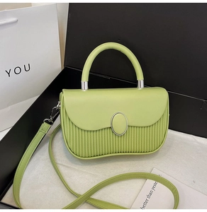 Detail view of grass green pleated leather bag with an oval silver buckle in gift box