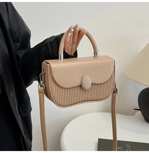 Detail of a beige handbag with pleated design and metal buckle held by a model