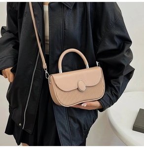 Detail of beige pleated leather crossbody bag featuring a unique oval metal buckle decoration